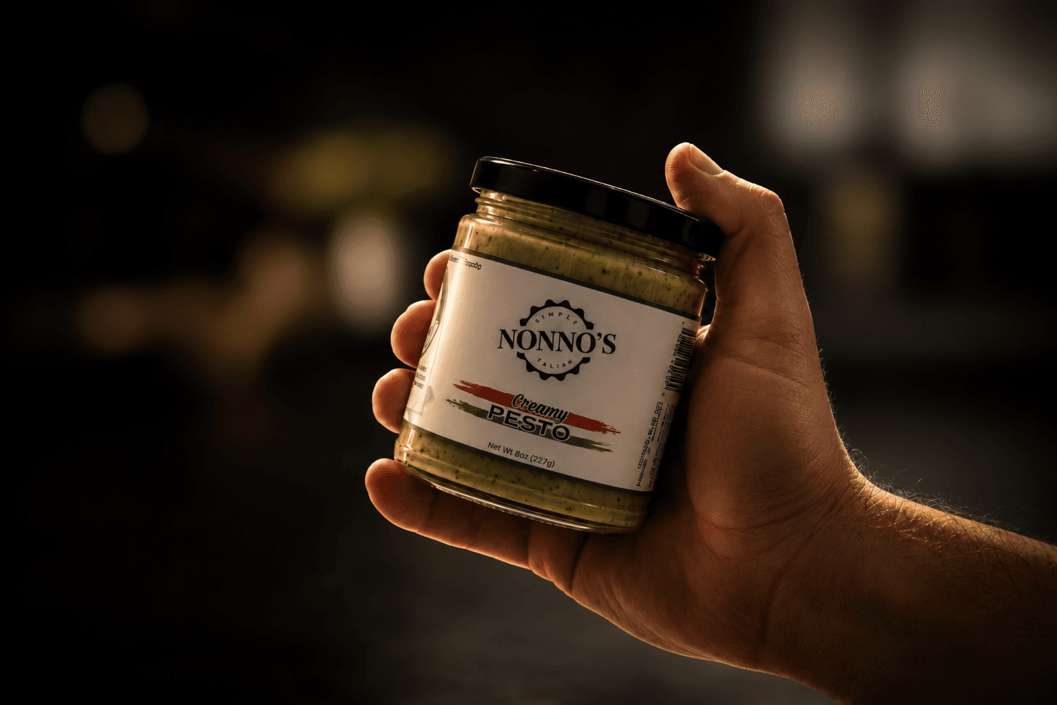 A hand pouring Simply Nonno's Creamy Pesto from its Net Wt. 8 oz (227 g) jar